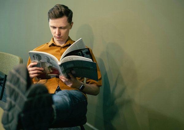 Young man in casual attire reading a magazine indoors, embodying a relaxed and studious vibe.