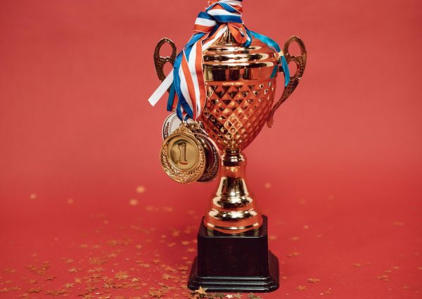 Golden trophy adorned with medals on a red backdrop surrounded by scattered confetti.